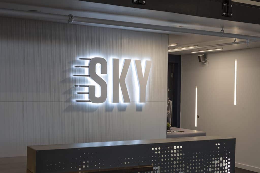 Illuminated "SKY" sign on a white wall in a modern, minimalist space with subtle lighting accents.