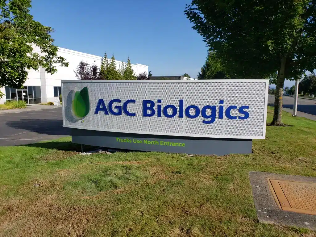 AGC Monument Sign Sign reading "AGC Biologics" with an adjacent logo in a business park, surrounded by grass and trees.