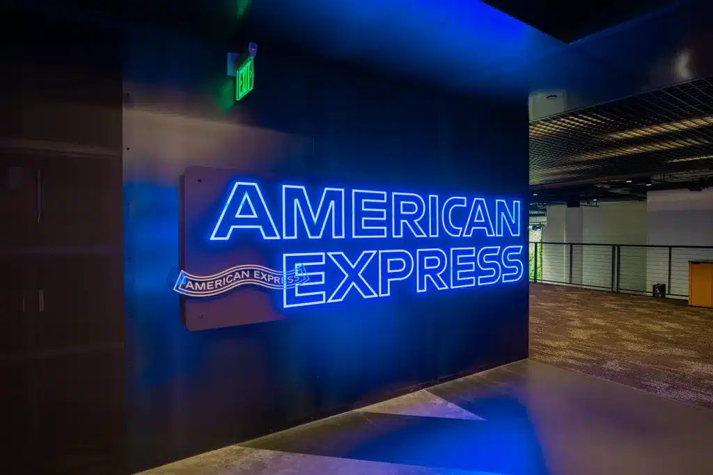 Neon blue "American Express" sign on a dark wall in a dimly lit interior space.