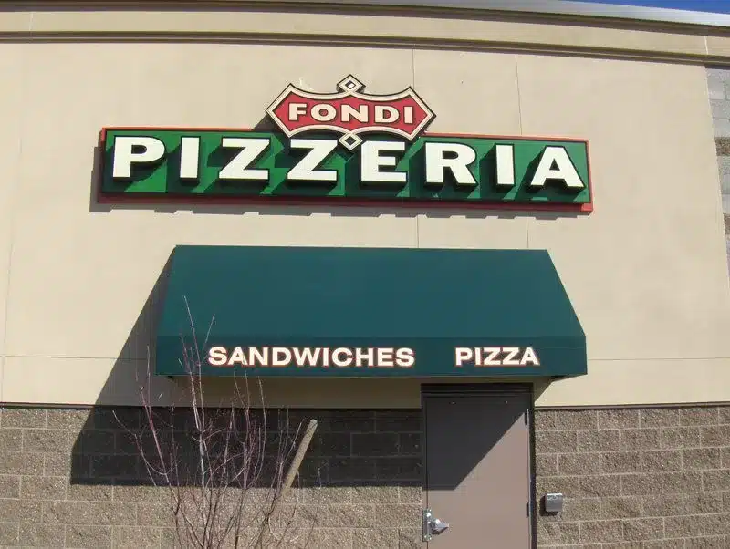 Pizzeria storefront with "Fondi Pizzeria" sign and a green awning displaying "Sandwiches Pizza. Pizzeria storefront with "Fondi Pizzeria" sign and a green awning displaying "Sandwiches Pizza.