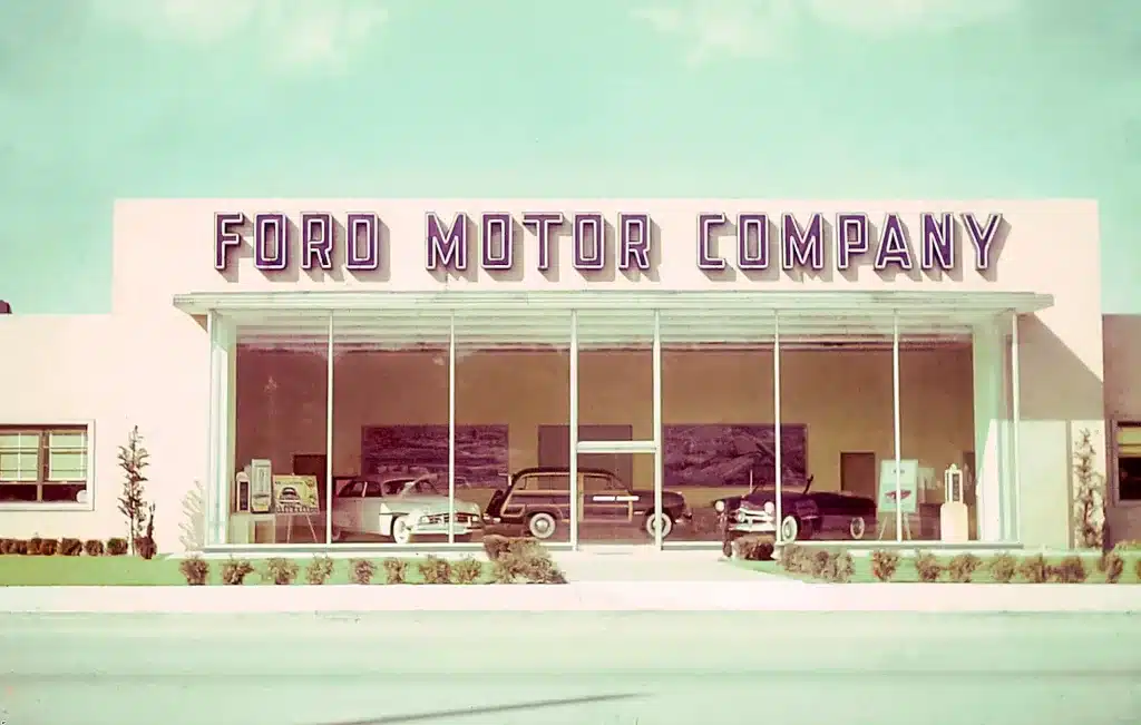 Vintage Ford Motor Company dealership with cars displayed through large glass windows in a 1960s architectural style. Vintage Ford Motor Company dealership with cars displayed through large glass windows in a 1960s architectural style.
