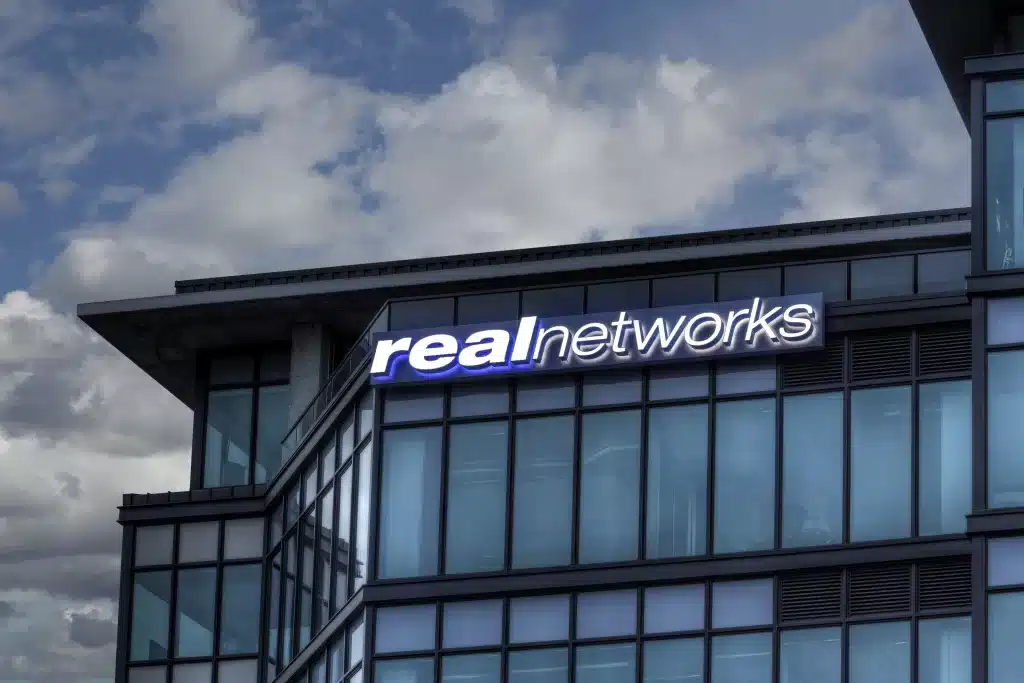 Building facade with "real networks" sign on top, set against a partly cloudy sky.