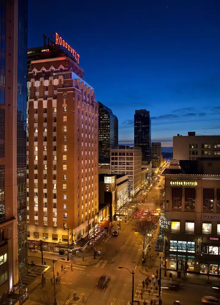 Night view of a city street with the illuminated Roosevelt Hotel on the left and various buildings alongside. Night view of a city street with the illuminated Roosevelt Hotel on the left and various buildings alongside.