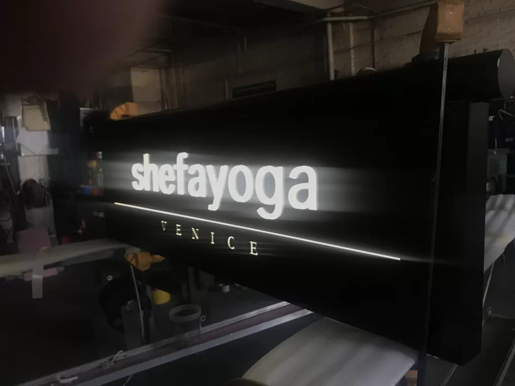 Illuminated sign reading "shefayoga VENICE" in a dimly lit environment. Illuminated sign reading "shefayoga VENICE" in a dimly lit environment.