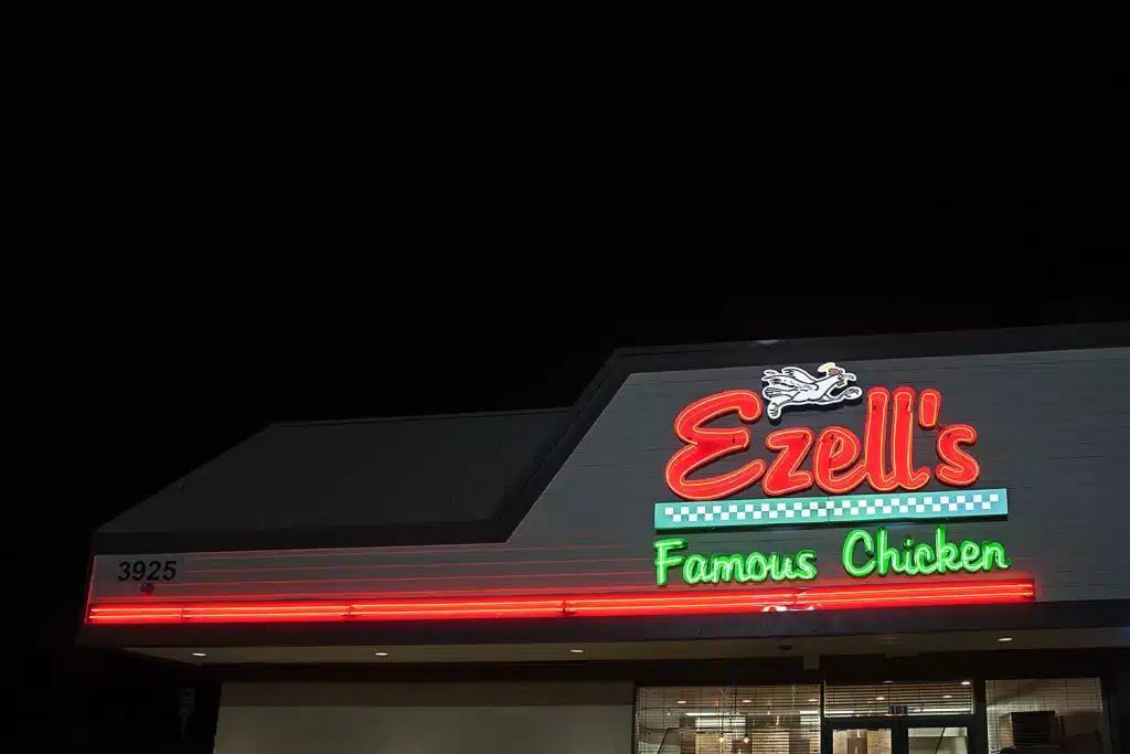 A lit restaurant sign reads "Ezell's Famous Chicken" at night with a small logo of a chicken.